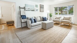 A modern living room with a grey sofa, two armchairs, a coffee table, and a large window with a city view.