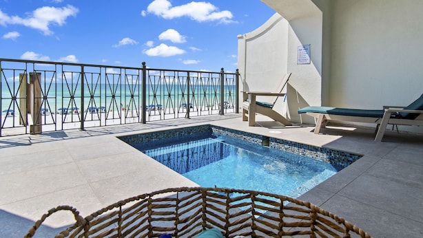 A pool area with a view of the beach, a lounge chair, and a small pool.