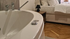 A modern bathroom with a large bathtub, a mirror, and a small table with a lamp. - Fera (Belgrade)