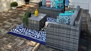 Un patio con mobiliario de mimbre, un paraguas grande y una cerca blanca.