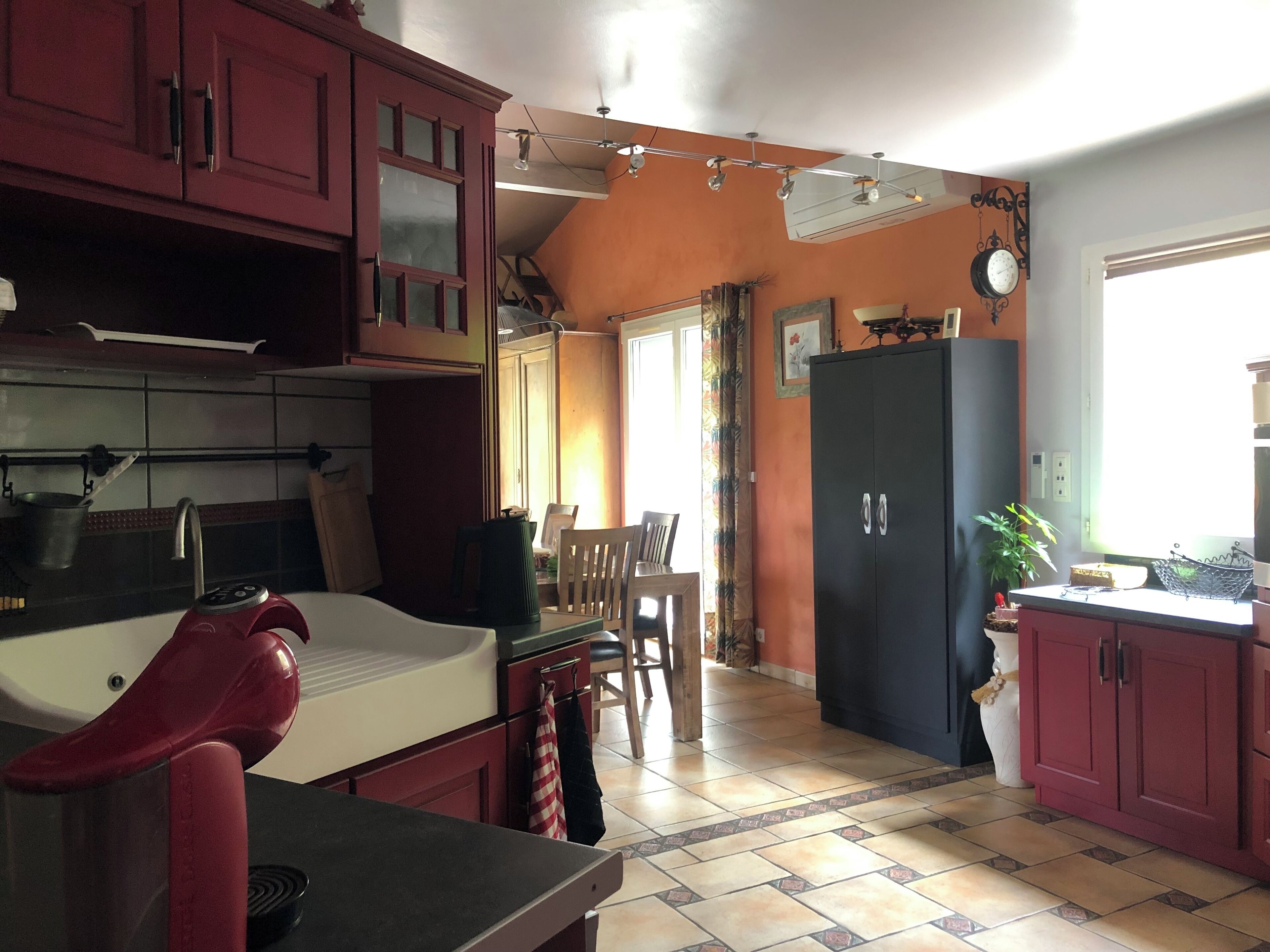 A kitchen with red cabinets, a sink, a stove, and a dining area with a table and chairs.