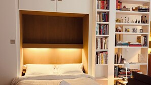 A neatly made bed with a rolled towel, a bookshelf filled with books and decorative items, and a wooden headboard. - An Attractive flat near by St-Germain, Le Bon Marché (Paris)
