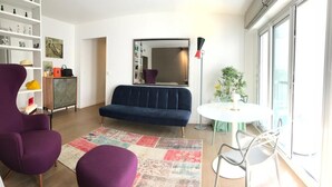 A living room with a dark blue sofa, purple armchairs, a white round table, and a large mirror. - An Attractive flat near by St-Germain, Le Bon Marché (Paris)