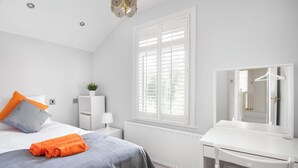 Une chambre à coucher comprenant un lit, une table de chevet avec une lampe, une commode, un miroir et une fenêtre avec des volets.