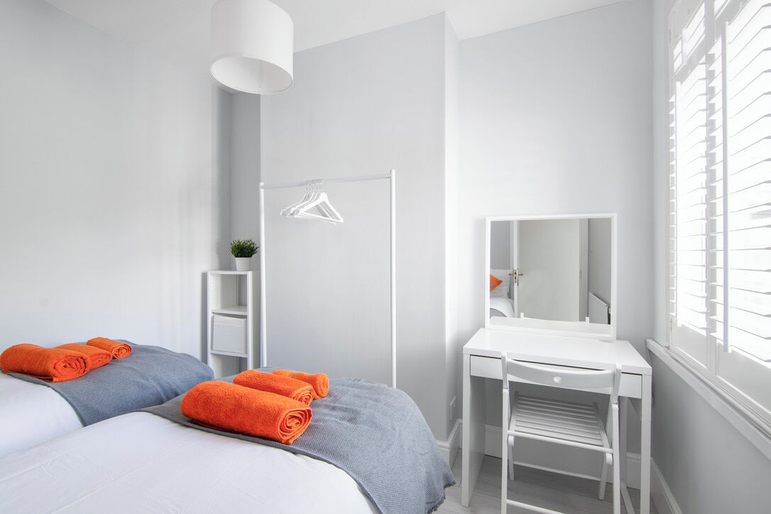 A modern bedroom with a bed, a bedside table, a mirror, and a window with blinds.