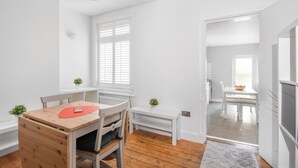 Une pièce lumineuse et blanche, avec une table et des chaises en bois, un petit banc et un radiateur.