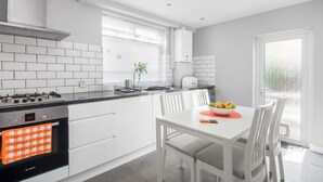 Une cuisine moderne avec des armoires blanches, un four Bosch et un coin repas comprenant une table et des chaises.