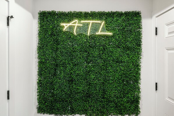 Un mur dont la texture évoque des feuilles vertes, sur lequel est apposée une enseigne au néon qui épelle le mot « ATL ».