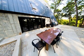 A modern outdoor dining area with a long table and chairs, a stone wall, and a metal roof. - Modern A-Frame Lake Cabin w/ Pickleball Ct.4Bd 3Ba (Genoa City)