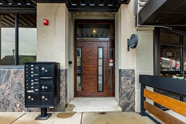 A building entrance with a wooden door, a mailbox, and a bench outside.