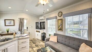 A modern kitchen with a built-in oven, a dining area with a sofa, and a large window with blinds.