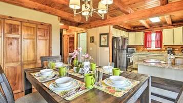 A wooden dining table set with plates, cups, and cutlery, with a chandelier above.