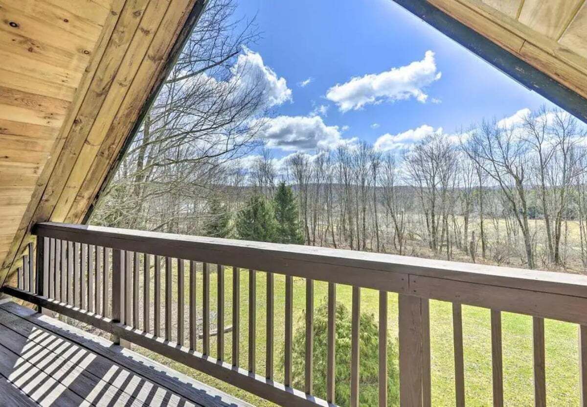 A wooden deck with a railing, overlooking a landscape with trees and a clear sky.