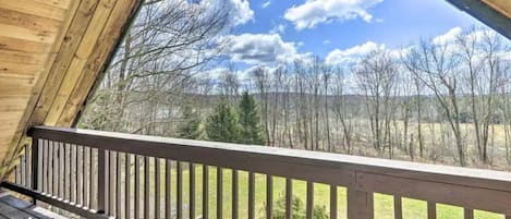 A wooden deck with a railing, overlooking a landscape with trees and a clear sky.