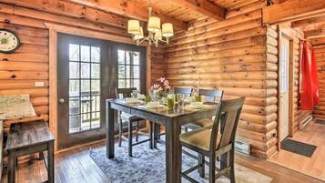 A log cabin interior with a dining table set for four, a chandelier, and a large window.