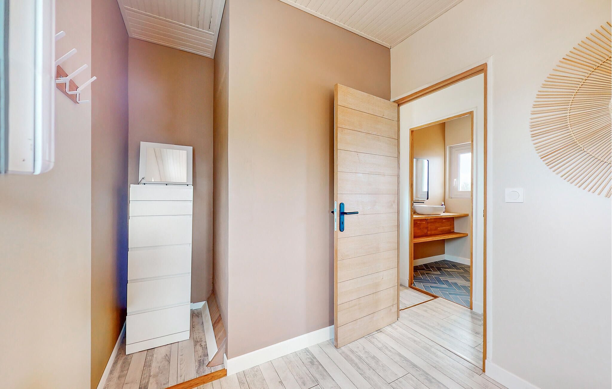 A hallway with a wooden door leading to a bathroom with a sink and mirror.