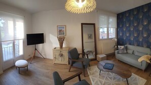 A living room with a sofa, chairs, a coffee table, a TV, and a decorative light fixture. - Elegant duplex, 75 meters from the Cathedral. Tourist or business stays (Amiens)
