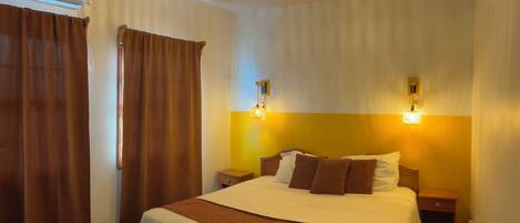 A hotel room with a large bed, two bedside tables, a nightstand, a wall-mounted lamp, and a ceiling light fixture.