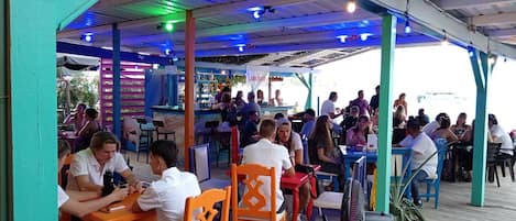 Un espacio exterior para comer con mesas y sillas, un bar y vistas al mar.