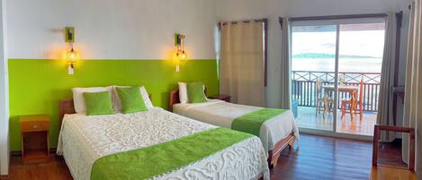 A hotel room with two beds, a balcony with a view of the sea, and a wooden floor.