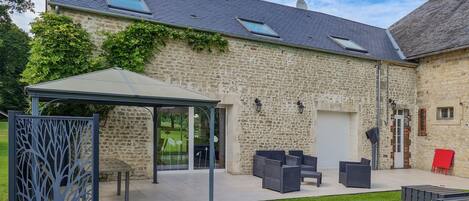 A stone building with a covered patio area, outdoor seating, and a garden.