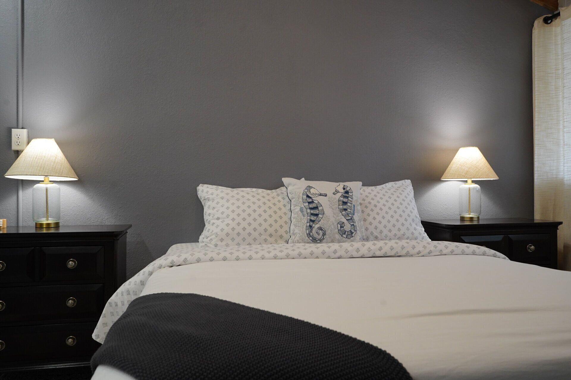Een hotelkamer met een bed, twee nachtkastjes met lampen, een gestreept kussen en een donker nachtkastje.