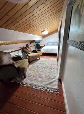 Un dormitorio acogedor en el ático con techo de madera, una cama, una silla y un escritorio.