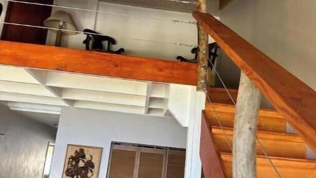 Un escalier en bois mène à une mezzanine équipée d’un ventilateur de plafond et d’une porte ornée d’un panneau décoratif.