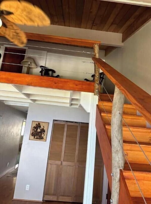 Una escalera de madera que sube a un entrepiso con ventilador de techo y una puerta con panel decorativo.