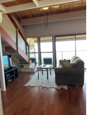 A spacious living area with a wooden staircase, a sofa, a coffee table, and a television.