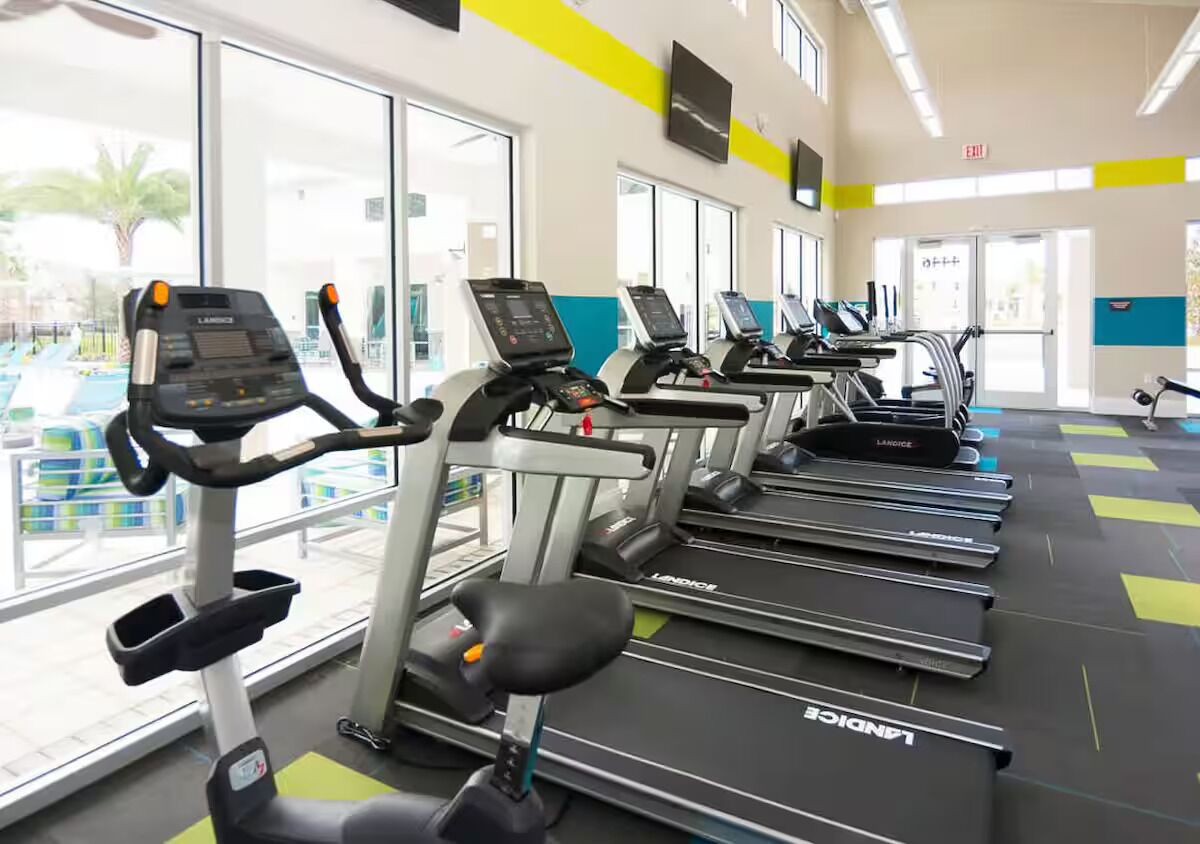 Une salle de sport équipée de plusieurs tapis de course, de grandes fenêtres et offrant une vue sur l’espace piscine.