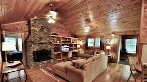 A cozy cabin interior with a stone fireplace, wooden walls, a sofa, and a television. - Trails End, your own private retreat in the Smokies! (Townsend)