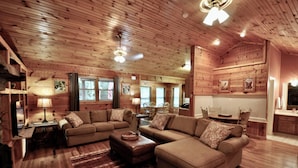 A cozy living room with wooden walls and ceiling, a large sectional sofa, a dining table with chairs, and a kitchen area. - Trails End, your own private retreat in the Smokies! (Townsend)
