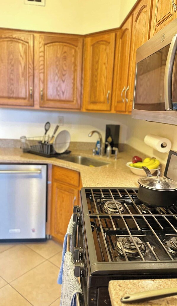 A kitchen with wooden cabinets, a stainless steel sink, a stove, and a microwave.