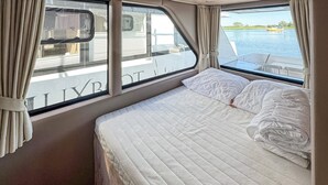 Un lit avec un matelas et des oreillers matelassés, une fenêtre avec des rideaux et une vue sur une étendue d’eau.