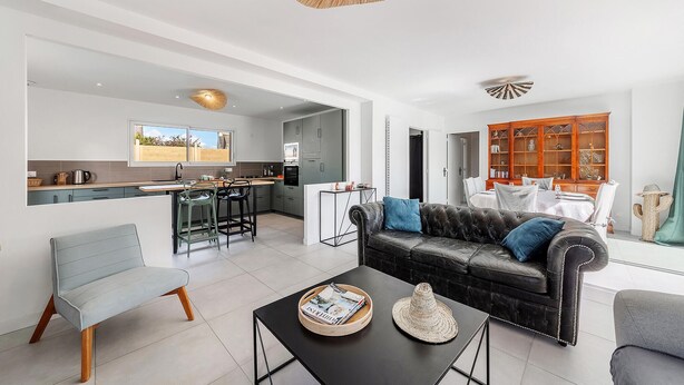 A modern living room with a black leather sofa, a grey armchair, and a coffee table with magazines and a hat.