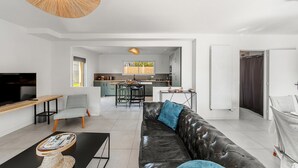 A modern living room with a leather sofa, a dining area, and a kitchen in the background.