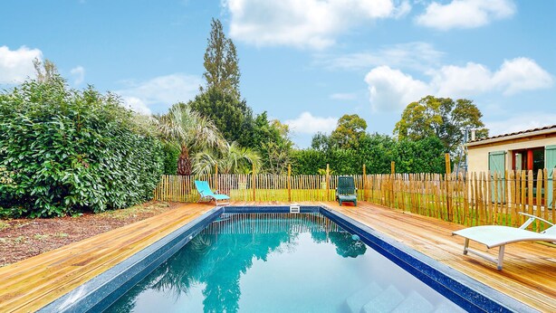 A rectangular swimming pool with a wooden deck surrounding it, a wooden fence, and a small building with a window. - Beautiful home in Rioux (Rioux)