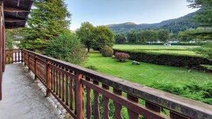 A balcony with a wooden railing overlooking a well-maintained garden and a distant mountain range.