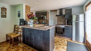 A modern kitchen with a central island, a dining area with a wooden chair, and a refrigerator.