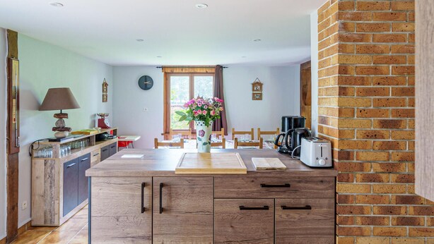 A kitchen with a wooden island, a brick wall, and a window with curtains.