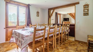 A dining area with a long wooden table set for four, wooden chairs, and a view through a window.