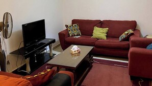 Ein Wohnzimmer mit einem roten Sofa, einer schwarzen Unterhaltungseinheit, einem Couchtisch und einem Standventilator.
