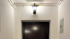 Eine dunkle Holztür mit einem runden Griff, weißen Wänden und einer Lampe darüber.