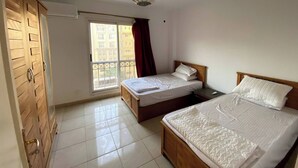 Ein Schlafzimmer mit zwei Betten, einem Kleiderschrank, einem Fenster mit Blick auf Gebäude und einer Deckenleuchte.