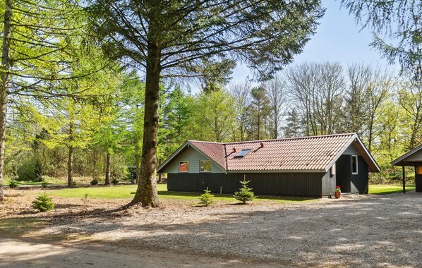 A rustic cabin with a sloped roof, surrounded by a forest.