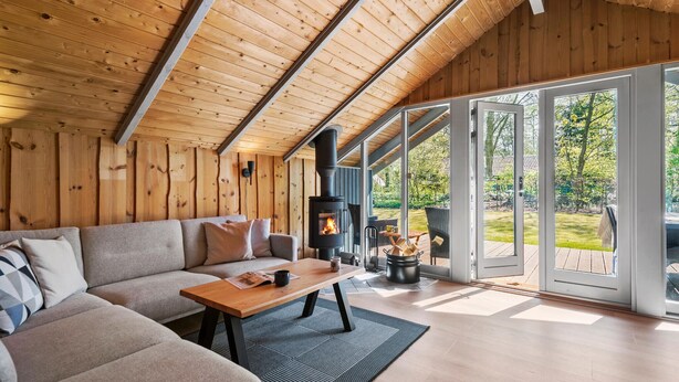 Een gezellige woonkamer met een houten plafond, een bank, een bijzettafeltje en een open haard.
