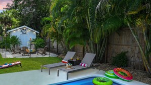 A backyard with a swimming pool, lounge chairs, a small shed, and a wooden fence.