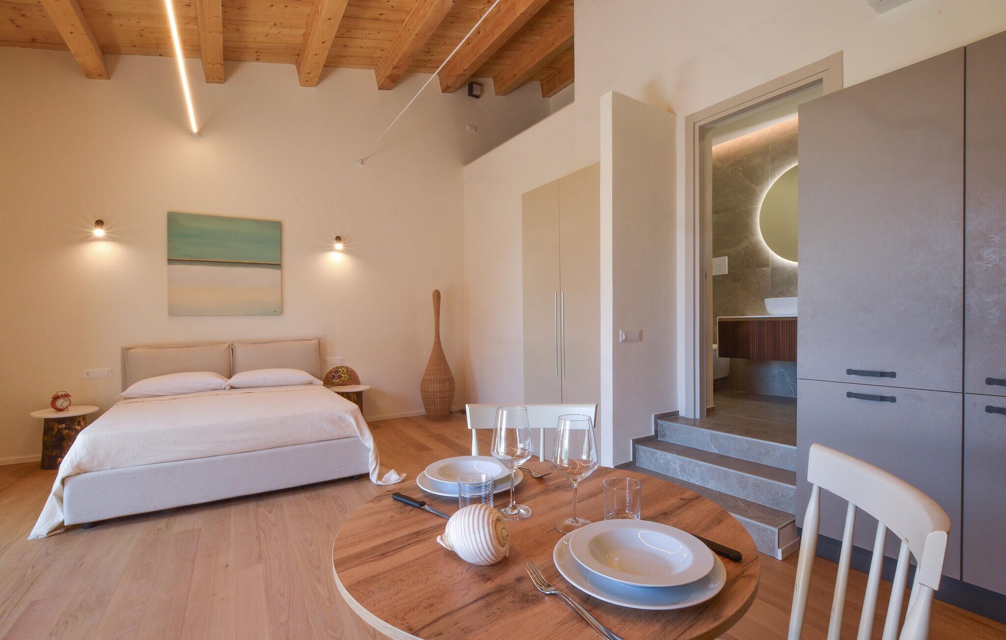 A bedroom with a bed, bedside table, and a dining table set for two with plates, glasses, and a vase.