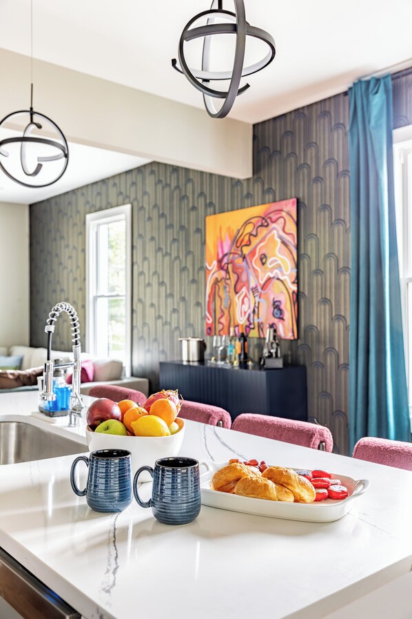 A modern kitchen with a marble countertop, two blue mugs, a fruit bowl, and a plate of croissants.